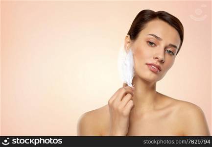 people and beauty concept - beautiful woman with feather touching her face skin over beige background. beautiful woman with feather touching her face