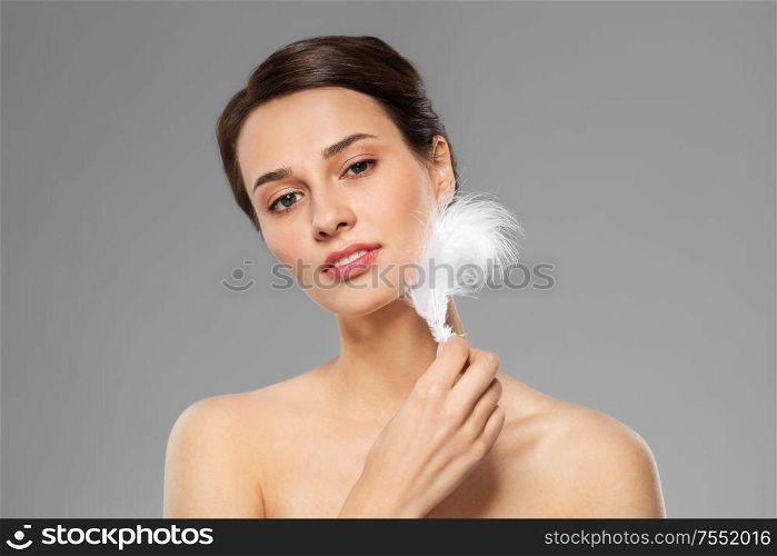 people and beauty concept - beautiful woman with feather touching her face skin over grey background. beautiful woman with feather touching her face