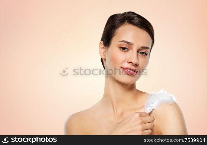 people and beauty concept - beautiful woman with feather touching her shoulder skin over beige background. beautiful woman with feather touching her shoulder