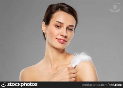 people and beauty concept - beautiful woman with feather touching her shoulder skin over grey background. beautiful woman with feather touching her shoulder