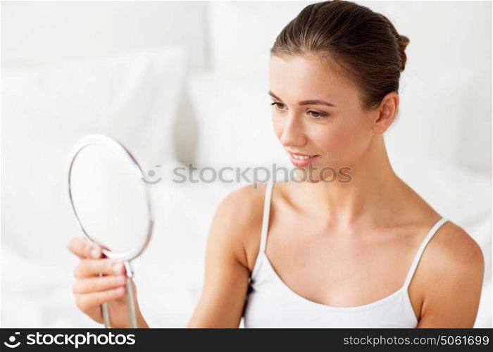 people and beauty concept - beautiful woman with mirror sitting on bed at home bedroom. beautiful woman with mirror sitting on bed at home