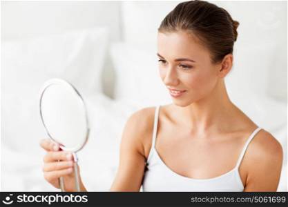 people and beauty concept - beautiful woman with mirror sitting on bed at home bedroom. beautiful woman with mirror sitting on bed at home