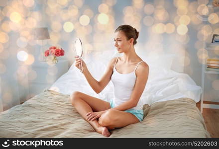 people and beauty concept - beautiful woman with mirror sitting on bed at home bedroom. beautiful woman with mirror sitting on bed at home