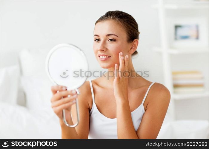 people and beauty concept - beautiful woman with mirror touching her face skin at home bedroom. beautiful woman with mirror touching her face skin
