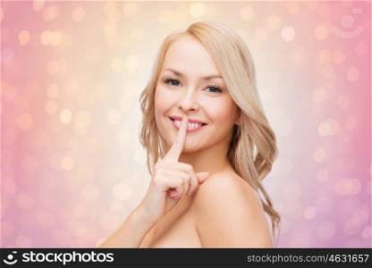 people and beauty concept - beautiful young woman with finger at her lips over rose quartz and serenity lights background. beautiful young woman with finger at her lips