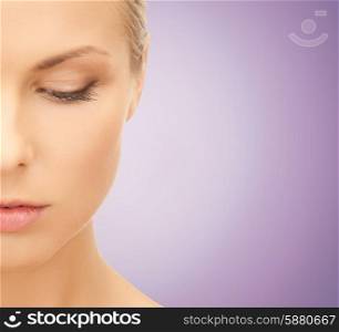 people and beauty concept - close up of beautiful young woman half face looking down over violet background