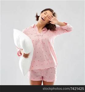 people and bedtime concept - happy sleepy yawning young woman in pajama holding pillow over grey background. sleepy yawning young woman in pajama with pillow