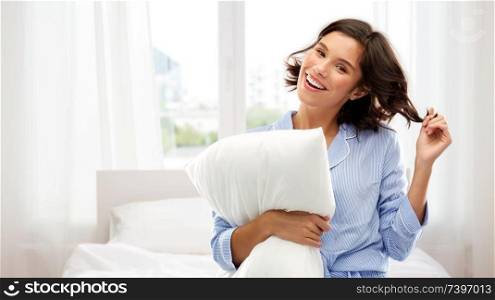 people and bedtime concept - happy young woman in pajama hugging pillow over background. happy woman in pajama with pillow over bedroom