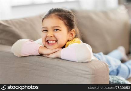people and childhood concept - happy smiling little girl lying on sofa at home. happy smiling little girl lying on sofa at home