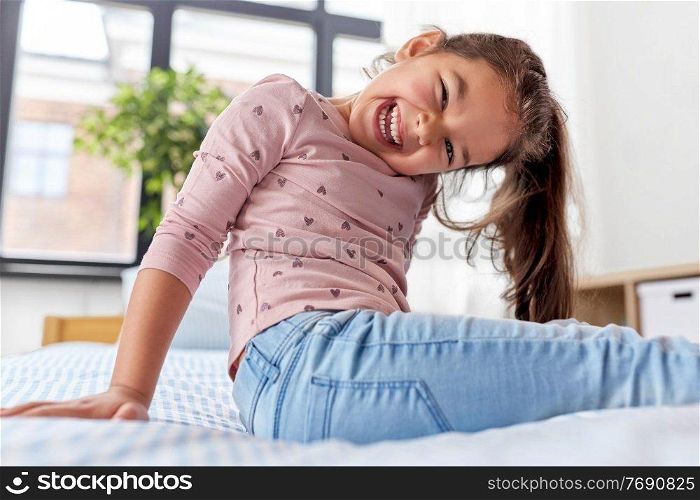people and childhood concept - happy smiling little girl sitting on bed at home. happy smiling little girl sitting on bed at home