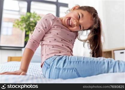 people and childhood concept - happy smiling little girl sitting on bed at home. happy smiling little girl sitting on bed at home