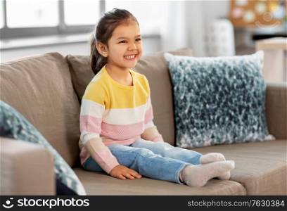 people and childhood concept - happy smiling little girl sitting on sofa at home. happy smiling little girl sitting on sofa at home
