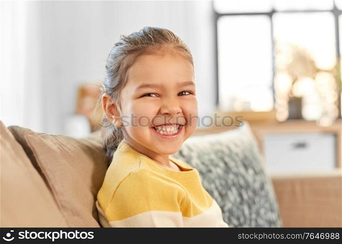 people and childhood concept - happy smiling little girl sitting on sofa at home. happy smiling little girl sitting on sofa at home