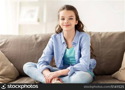 people and childhood concept - happy smiling preteen girl sitting on sofa at home. happy smiling preteen girl sitting on sofa at home