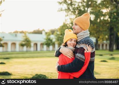 People and closeness concept. Young couple in love have date, embrace each other, feel support, being alone in park, have perfect relationships. Handsome man in warm sweater and hat hugs girlfriend