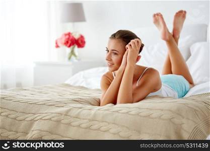 people and comfort concept - happy young beautiful woman lying on bed at home bedroom. happy young woman lying on bed at home