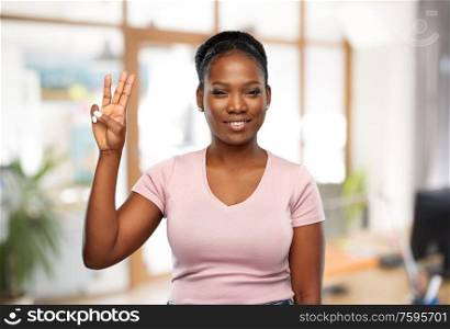people and corporate concept - happy smiling african american young woman showing three fingers over office background. african woman showing three fingers at office
