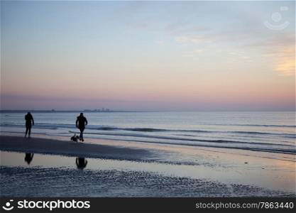 people and dog on beach at sundown on the North Sea cost of the netherlands with silhouette of Zandvoort in the background