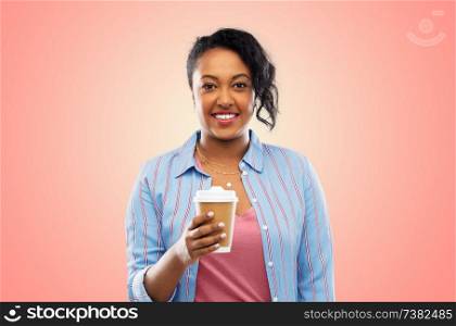people and drinks concept - happy african american young woman drinking takeaway coffee from paper cup over living coral background. happy african american woman drinking coffee