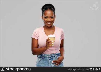 people and drinks concept - happy african american young woman drinking takeaway coffee from paper cup over grey background. happy african american woman drinking coffee