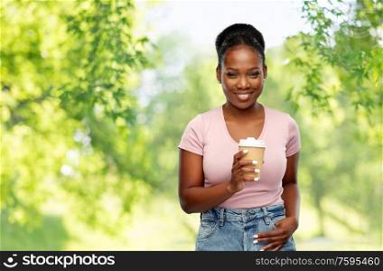 people and drinks concept - happy african american young woman drinking takeaway coffee from paper cup over green natural background. happy african american woman drinking coffee