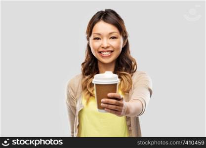 people and drinks concept - happy young asian woman drinking takeaway coffee from paper cup over grey background. happy asian woman drinking coffee