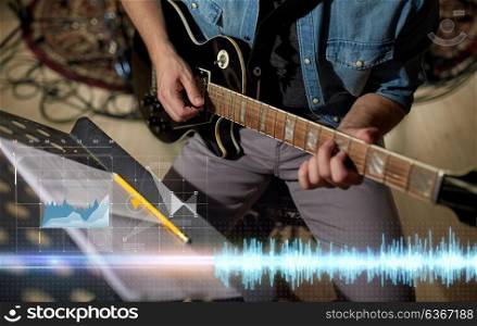 people and entertainment concept - male guitarist playing electric guitar with music book on stand at studio. man with music book on stand playing guitar