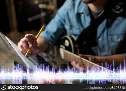 people and entertainment concept - man with guitar writing notes to music book at sound recording studio. musician with guitar and music book at studio