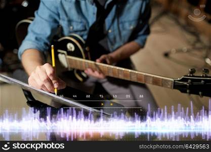 people and entertainment concept - man with guitar writing notes to music book at sound recording studio. musician with guitar and music book at studio
