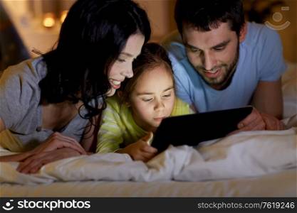 people and family concept - close up of happy mother, father and little daughter with tablet pc computer in bed at night at home. family with tablet pc in bed at night at home
