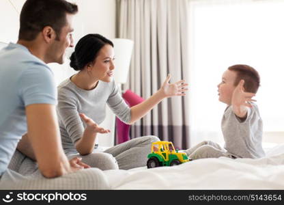 people and family concept - happy child with toy tractor and parents playing in bed at home or hotel room. happy family in bed at home or hotel room