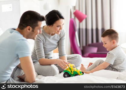 people and family concept - happy child with toy tractor and parents playing in bed at home or hotel room. happy family in bed at home or hotel room