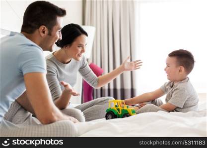 people and family concept - happy child with toy tractor and parents playing in bed at home or hotel room. happy family in bed at home or hotel room