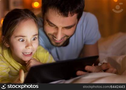 people and family concept - happy father and little daughter with tablet pc computer in bed at night at home. family with tablet pc in bed at night at home