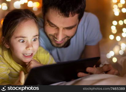 people and family concept - happy father and little daughter with tablet pc computer in bed at night at home. family with tablet pc in bed at night at home