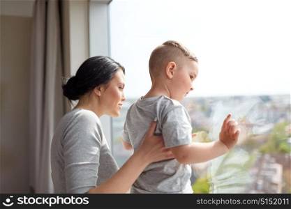 people and family concept - happy mother and little son looking through window at home. mother and son looking through window at home