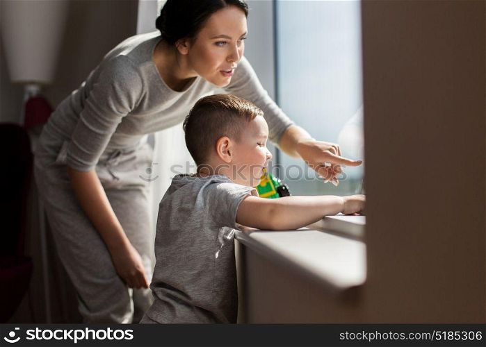 people and family concept - happy mother and little son with toy car looking through window at home. mother and son looking through window at home