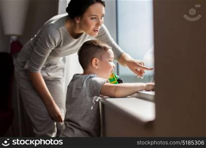 people and family concept - happy mother and little son with toy car looking through window at home. mother and son looking through window at home