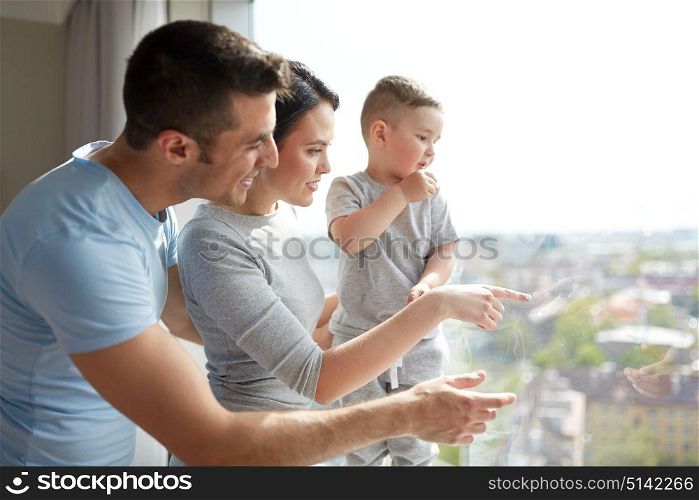 people and family concept - happy mother, father and little son looking through window at home. happy family looking through window at home