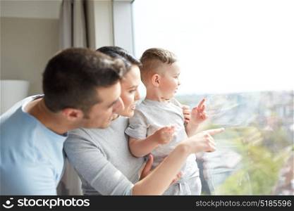 people and family concept - happy mother, father and little son looking through window at home. happy family looking through window at home