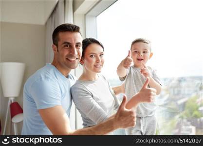 people and family concept - happy mother, father and little son showing thumbs up at home window. happy family at window