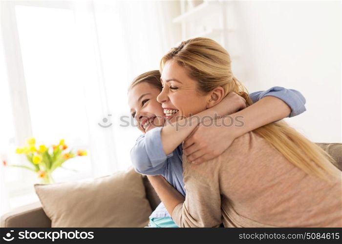 people and family concept - happy smiling girl with mother hugging on sofa at home. happy smiling family hugging on sofa at home. happy smiling family hugging on sofa at home