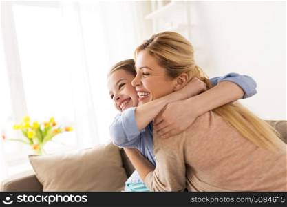 people and family concept - happy smiling girl with mother hugging on sofa at home. happy smiling family hugging on sofa at home. happy smiling family hugging on sofa at home
