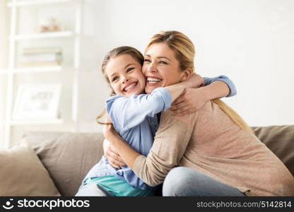 people and family concept - happy smiling girl with mother hugging on sofa at home. happy smiling family hugging on sofa at home