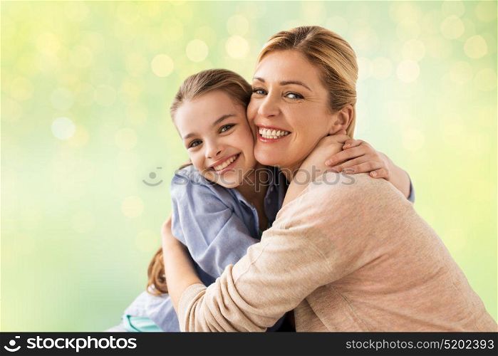 people and family concept - happy smiling girl with mother hugging over holidays lights background. happy girl with mother hugging over lights