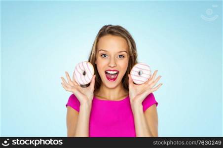 people and fast food concept - happy young woman or teen girl in pink dress with donuts over blue background. happy woman or teen girl with donuts