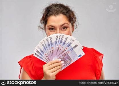 people and finances concept - happy woman in red dress hiding her face behind euro money banknotes over grey background. happy woman holding euro money banknotes