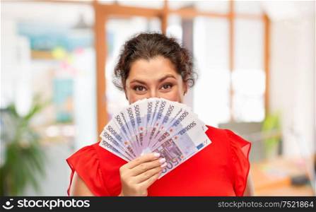 people and finances concept - happy woman in red dress hiding her face behind euro money banknotes over office background. happy woman holding euro money banknotes