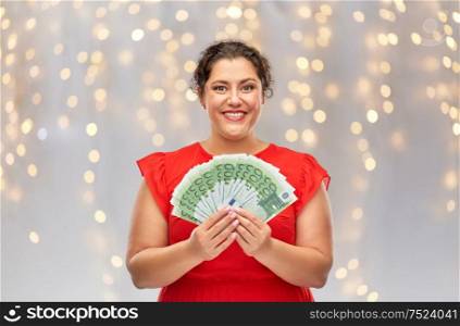 people and finances concept - happy woman in red dress holding hundreds of euro money banknotes over festive lights background. happy woman holding hundreds of money banknotes