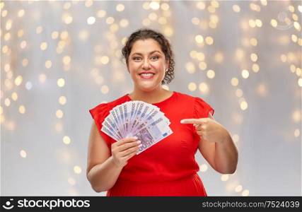 people and finances concept - happy woman in red dress showing euro money banknotes over festive lights background. happy woman showing euro money banknotes